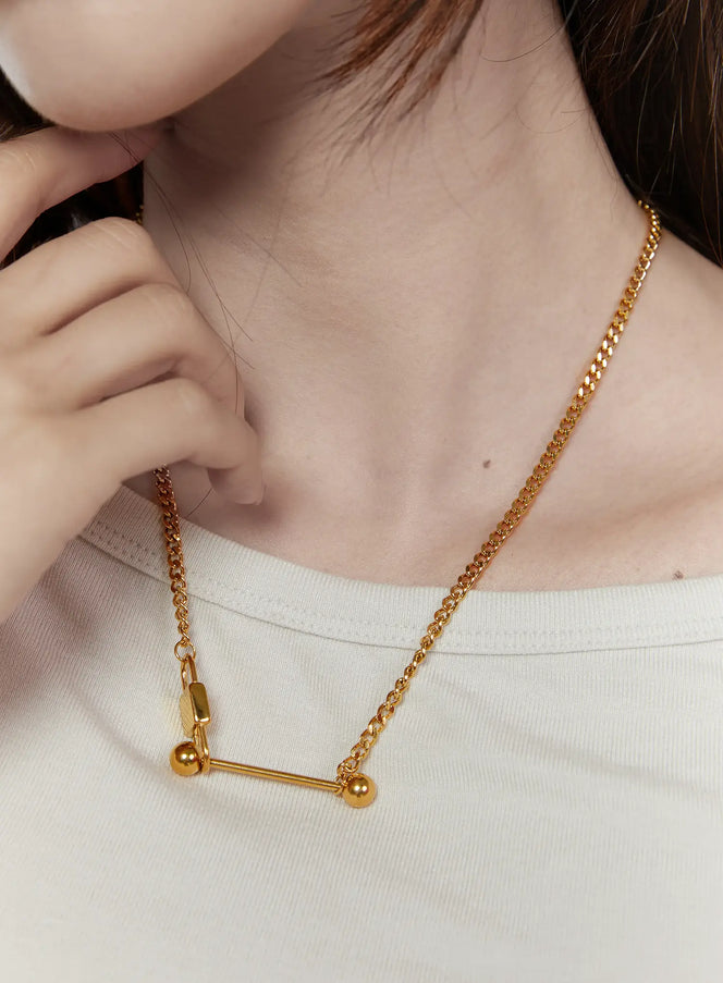 LEWKIN Titan Bar Necklace IL522 gold front close-up on model neck, bar pendant with ball ends on curb chain over white tee