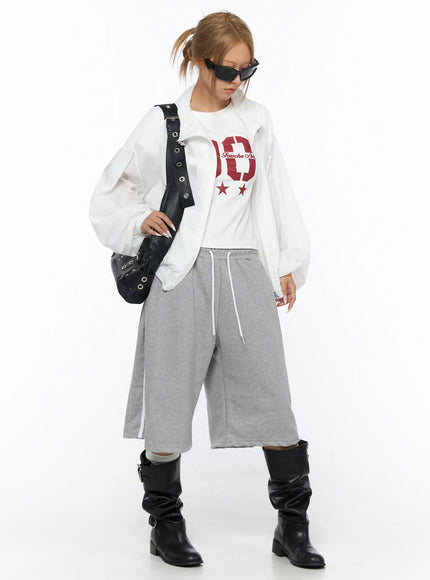 Track Bermuda Shorts CU523 Gray styled outfit front view on model with white jacket, graphic tee, black shoulder bag and sunglasses, sporty street look