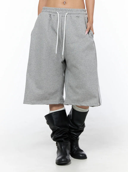 Track Bermuda Shorts CU523 Gray front close-up on model showing elastic drawstring waistband, wide-leg cut, side stripe detail, fleece fabric