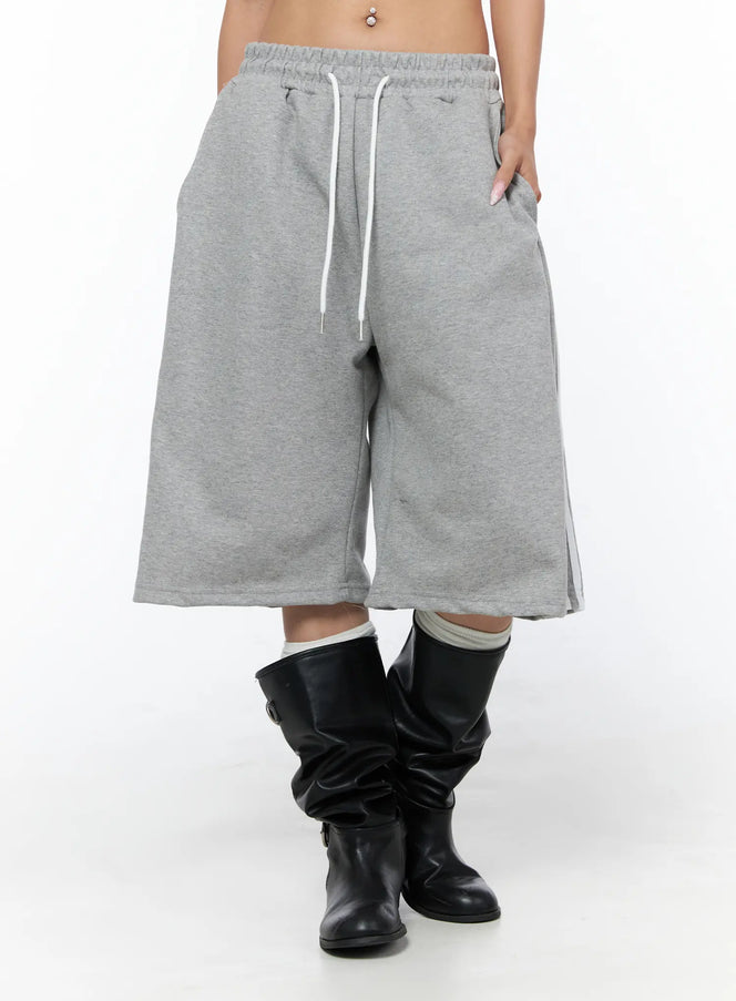 Track Bermuda Shorts CU523 Gray front close-up on model showing elastic drawstring waistband, wide-leg cut, side stripe detail, fleece fabric