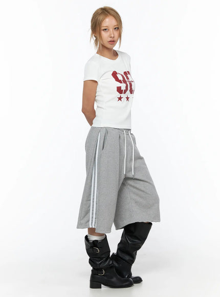 Track Bermuda Shorts CU523 Gray S/M side view on model wearing white graphic tee and black leather boots, wide-leg fleece shorts with white side stripes