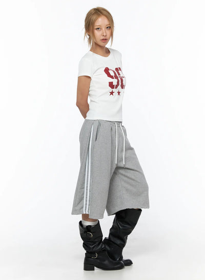Track Bermuda Shorts CU523 Gray S/M side view on model wearing white graphic tee and black leather boots, wide-leg fleece shorts with white side stripes