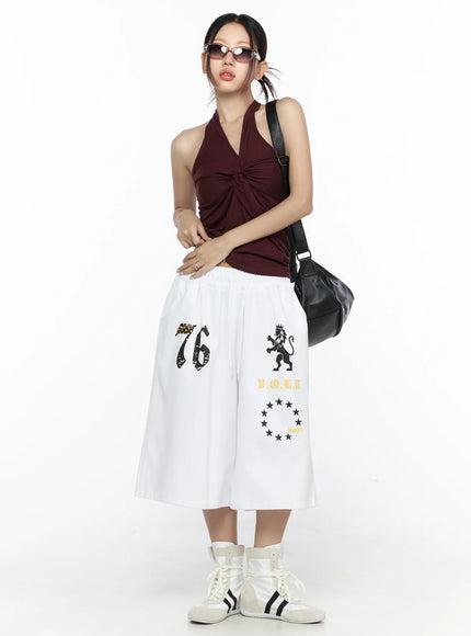 Twist Halter Top CL524 Dark red full-body front view on model with sunglasses and black bag showing complete outfit with white graphic wide-leg pants and sneakers
