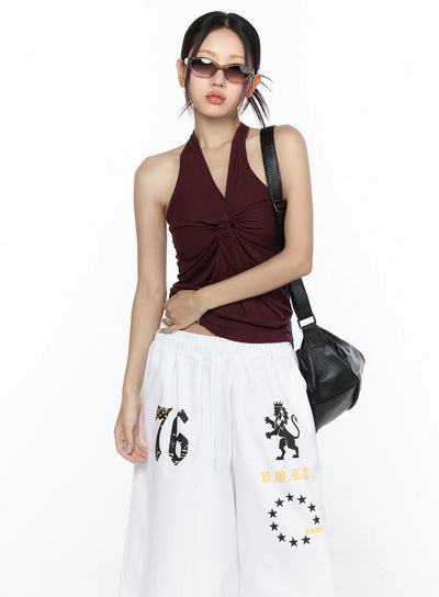 LEWKIN Twist Halter Top CL524 Dark red front view on model wearing sunglasses and black shoulder bag styled with white graphic wide-leg pants S/M