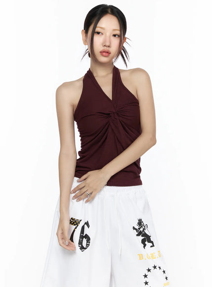 Twist Halter Top CL524 Dark red front view on model with arms relaxed showing V-neck twist knot center detail and soft draped silhouette with white graphic pants
