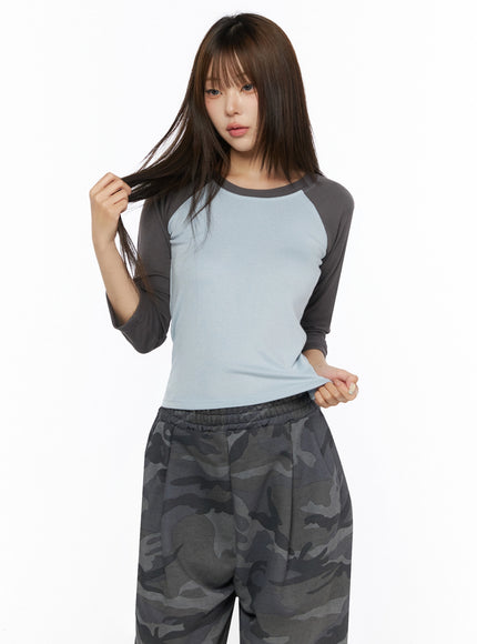 Two-Tone Long Sleeve Top IL523 Light blue three-quarter front shot on model touching hair, charcoal raglan sleeves and fitted cropped silhouette visible