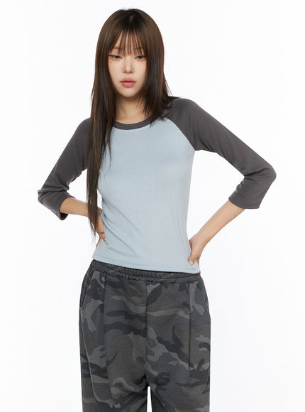 Two-Tone Long Sleeve Top IL523 Light blue front bust shot on model with hands on hips, showing light blue body and charcoal 3/4 raglan sleeves, cotton texture