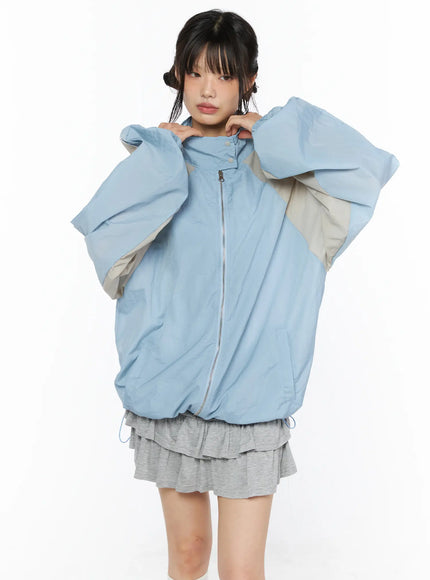 Two-Tone Oversized Windbreaker CU530 Light blue front close-up on model arms raised showing oversized silhouette center zipper and beige color-block panels