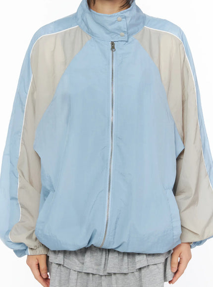 Two-Tone Oversized Windbreaker CU530 Light blue close-up front torso shot showing center zipper stand collar snap button and beige raglan color-block panel detail