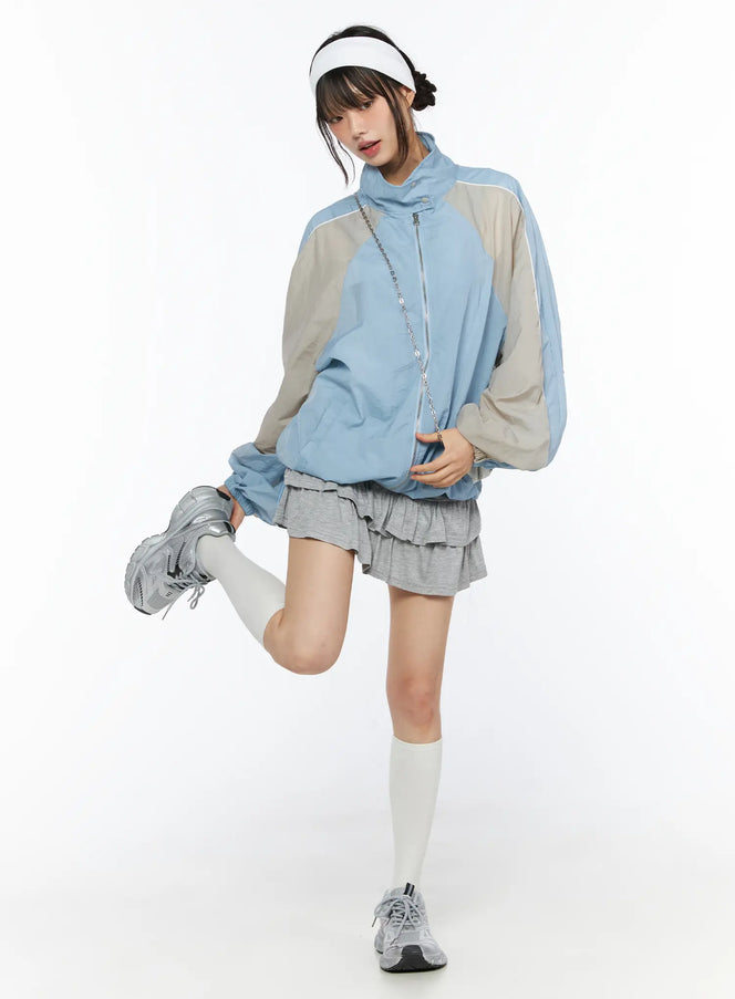 Two-Tone Oversized Windbreaker CU530 Light blue full-body front shot on model one leg raised wearing gray ruffle skirt white knee socks silver sneakers