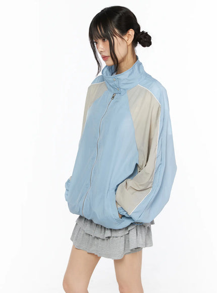 Two-Tone Oversized Windbreaker CU530 Light blue side shot on model standing relaxed showing beige contrast sleeve panel white piping trim and elasticated cuffs