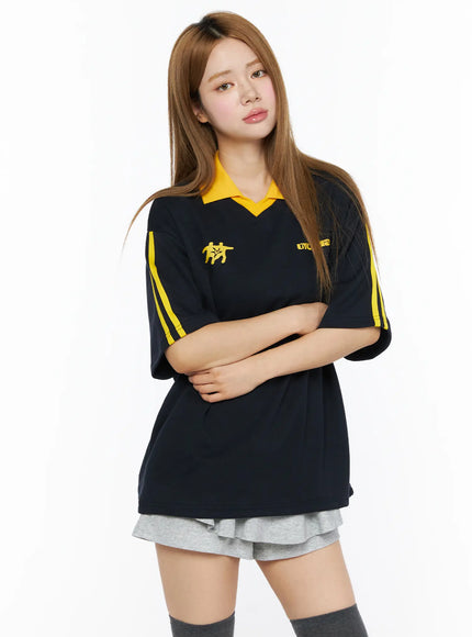 Two-Tone Relaxed-Fit Polo Shirt CL502 Dark blue front shot on model arms crossed showing yellow collar yellow sleeve stripes chest graphic and oversized relaxed fit silhouette