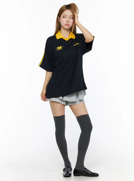 Two-Tone Relaxed-Fit Polo Shirt CL502 Dark blue front shot on model standing hand in hair showing yellow graphic print and oversized relaxed fit with grey shorts