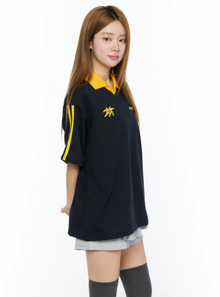 Two-Tone Relaxed-Fit Polo Shirt CL502 Dark blue angled front shot on model showing yellow V-neck collar yellow sleeve stripes and chest graphic print with grey shorts