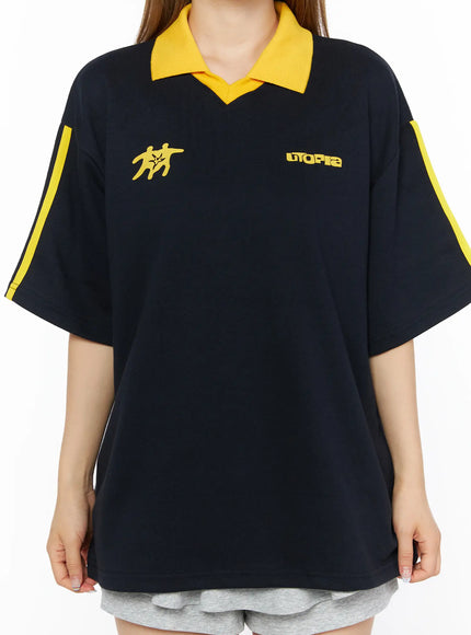 Two-Tone Relaxed-Fit Polo Shirt CL502 Dark blue close-up front torso shot on model showing yellow polo collar yellow figure graphic UTOPIA text and yellow sleeve stripes detail