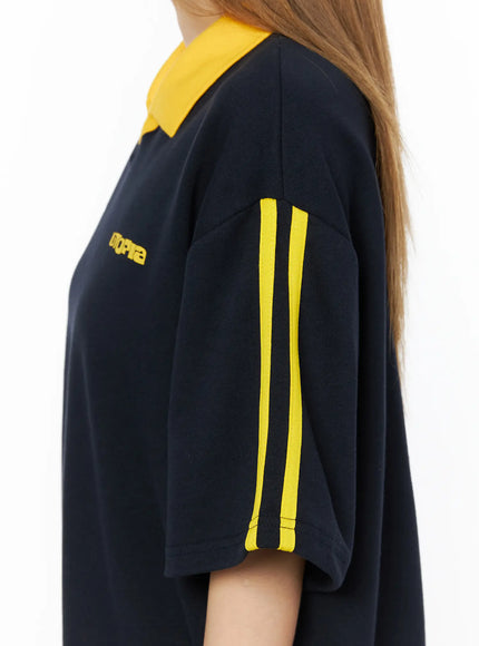 Two-Tone Relaxed-Fit Polo Shirt CL502 Dark blue detail close-up side shot showing yellow double stripe tape on sleeve shoulder seam and UTOPIA text on dark blue cotton fabric