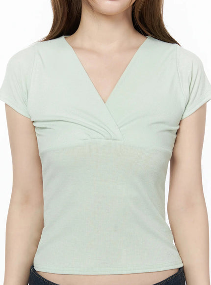 V-Neck Ruched Slim-Fit Top IU525 Light green close-up detail shot showing deep V-neck crossover ruched bust and ribbed stretch fabric texture on model