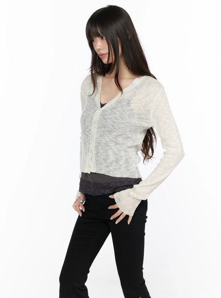 V-Neck Sheer Cardigan CL522 light beige angled front shot on model, sheer ribbed knit with V-neck buttons and flared cuffs, layered over lace top and black skinny pants