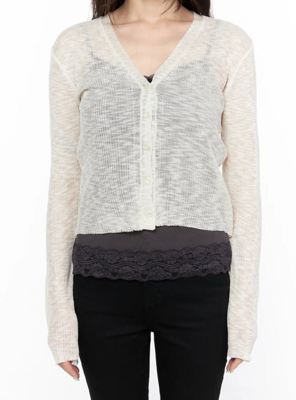 V-Neck Sheer Cardigan CL522 light beige close-up front shot on model, sheer ribbed knit with pearl-tone buttons, V-neckline, lace hem detail visible at hem, black pants