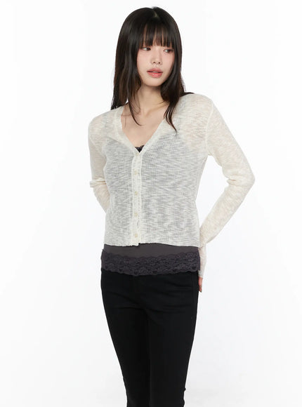 V-Neck Sheer Cardigan CL522 light beige front shot on model, cropped semi-sheer ribbed knit cardigan with V-neck and button front, layered over lace-trim top and black pants