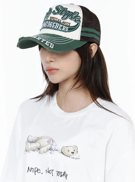 Vintage Graphic Cap IL506 Green three-quarter model shot, cap brim lowered over eyes, distressed green bill with white stitch lines, mesh back