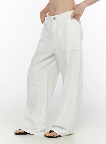 Wide Leg Cotton Pants CL521 White side view on model holding waistband, showing relaxed wide leg drape, patch pockets, and black thong sandals