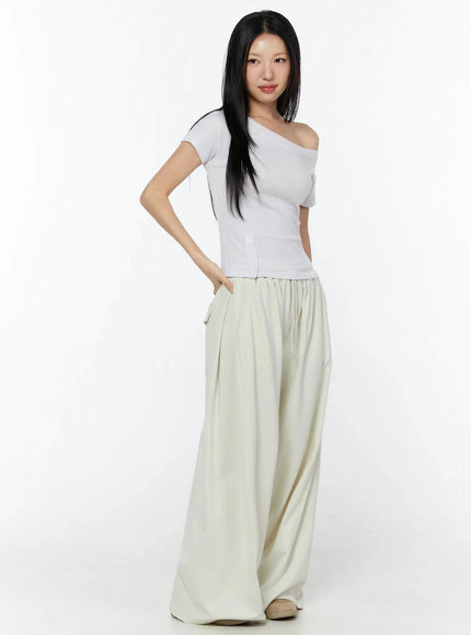 Wide Leg Sweatpants IU524 Light beige three-quarter front view on model with hand in pocket, paired with white asymmetric tee showing voluminous wide-leg drape