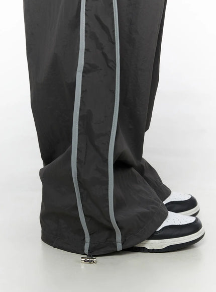 Wide Leg Track Pants CL501 Dark gray close-up detail of hem and ankle area showing reflective side stripe, drawstring toggle stopper, sneakers