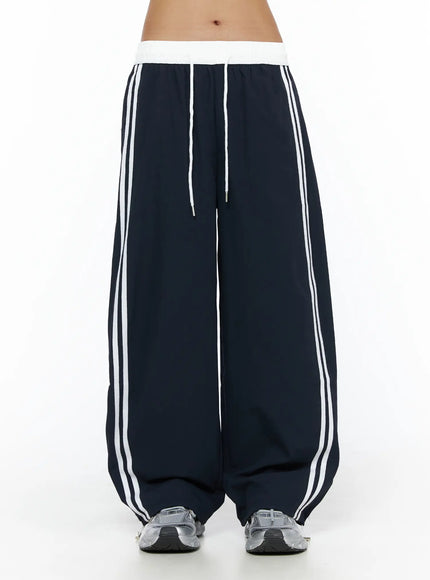 Wide Leg Track Pants CL503 Dark blue front close-up on model, white ribbed elastic waistband with drawstring, double white side stripes, wide-leg fit