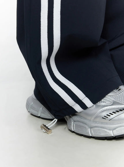 Wide Leg Track Pants CL503 Dark blue close-up detail of hem and ankle, double white side stripes, drawstring toggle at hem, silver sneakers styling