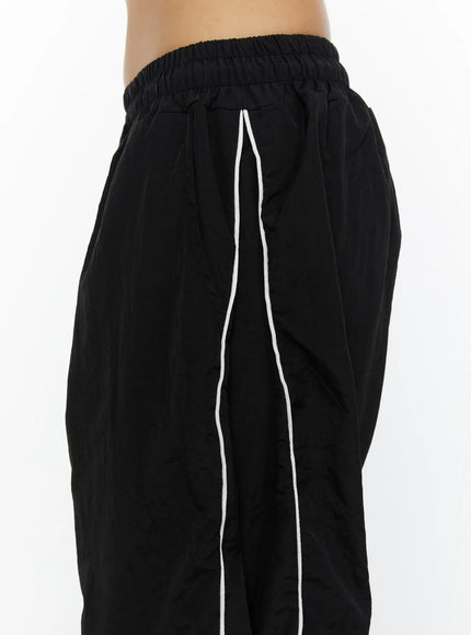 Wide-Leg Track Pants CL515 Black close-up detail shot of elastic waistband and white contrast seam piping on crinkled nylon fabric