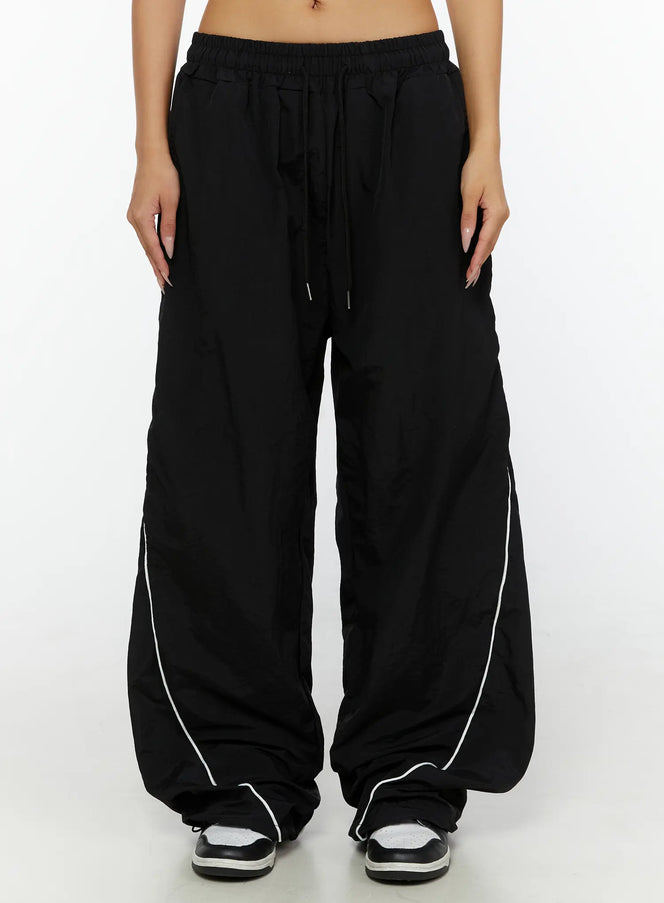 Wide-Leg Track Pants CL515 Black front close-up on model showing elastic drawstring waistband and wide-leg silhouette with white contrast piping
