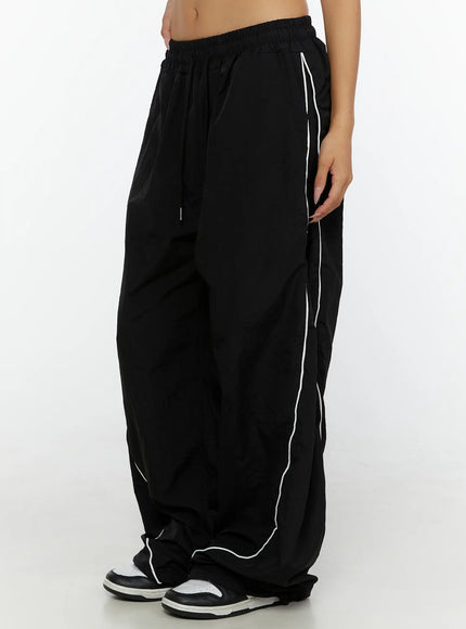 Wide-Leg Track Pants CL515 Black side close-up on model showing drawstring waistband white curved piping and gathered hem over sneakers