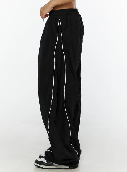 Wide-Leg Track Pants CL515 Black side shot on model highlighting white curved piping detail along leg and voluminous nylon fabric