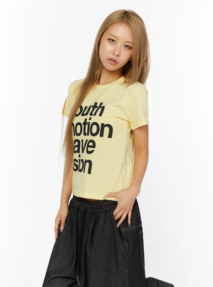 Youth Graphic Short Sleeve Tee IL524 Yellow side-angle front view on model, cropped cotton tee with bold black text print, styled with dark wide-leg denim