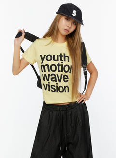 LEWKIN Youth Graphic Short Sleeve Tee IL524 Yellow front view on model wearing black cap and backpack, styled with wide-leg dark pants, S/M