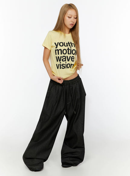 Youth Graphic Short Sleeve Tee IL524 Yellow full-body front view on model looking down, cropped tee paired with dark wide-leg drawstring denim pants