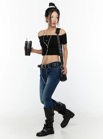 Zainab Low-Rise Flared Bootcut Jeans CU529 Dark blue full-body styled shot on model with bun, black crop top, studded belt, crossbody bag and knee-high boots
