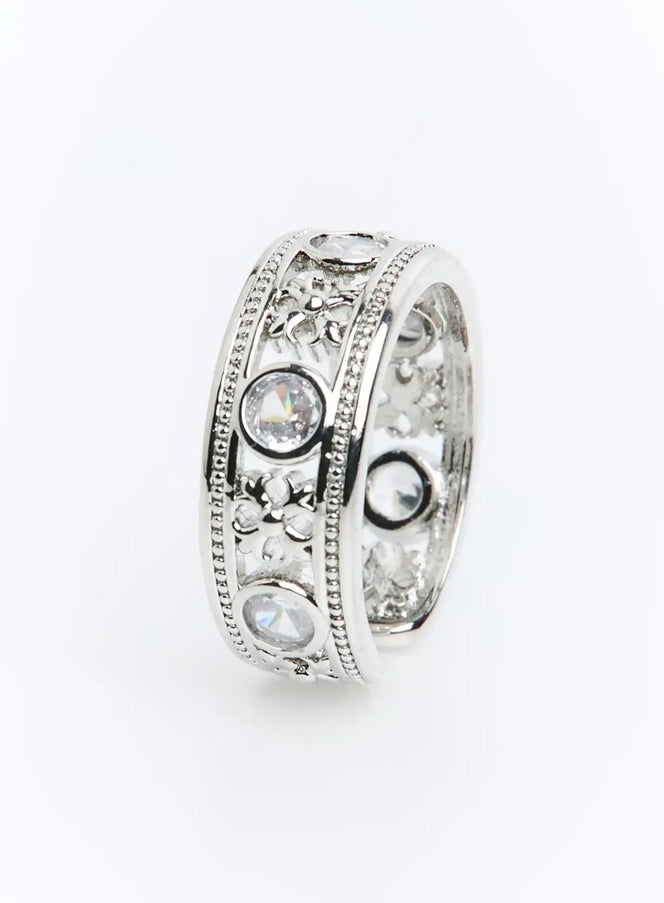 LEWKIN Calder Ring IU503 in silver, angled product shot showing wide band with bezel-set clear crystals, floral filigree cutwork, and milgrain bead edges.