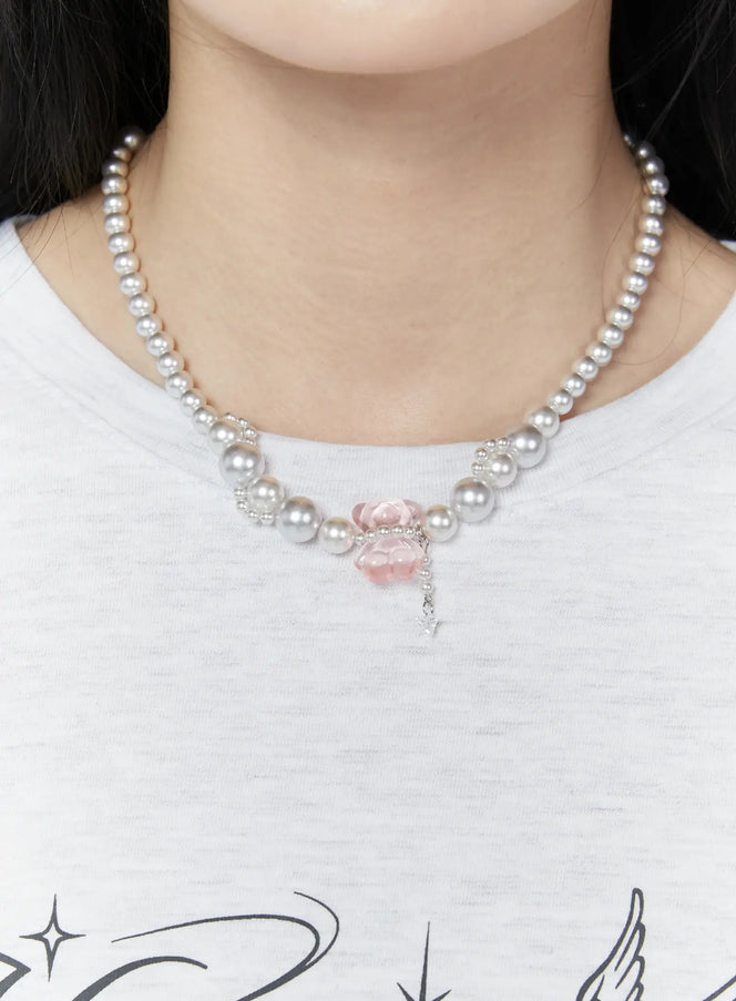 LEWKIN Cato Lovely Necklace IU503 in silver and pink, neck close-up on model, pearl strand with pink gummy bear bead and star charm pendant, worn over white graphic tee.