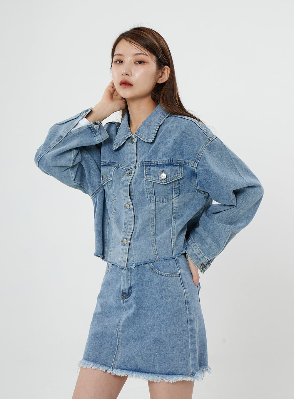 LEWKIN Sienna Crop Jeans Jacket CS21 in light blue, front three-quarter view on model, cropped cotton denim with chest pockets and silver buttons, paired with matching denim mini skirt.