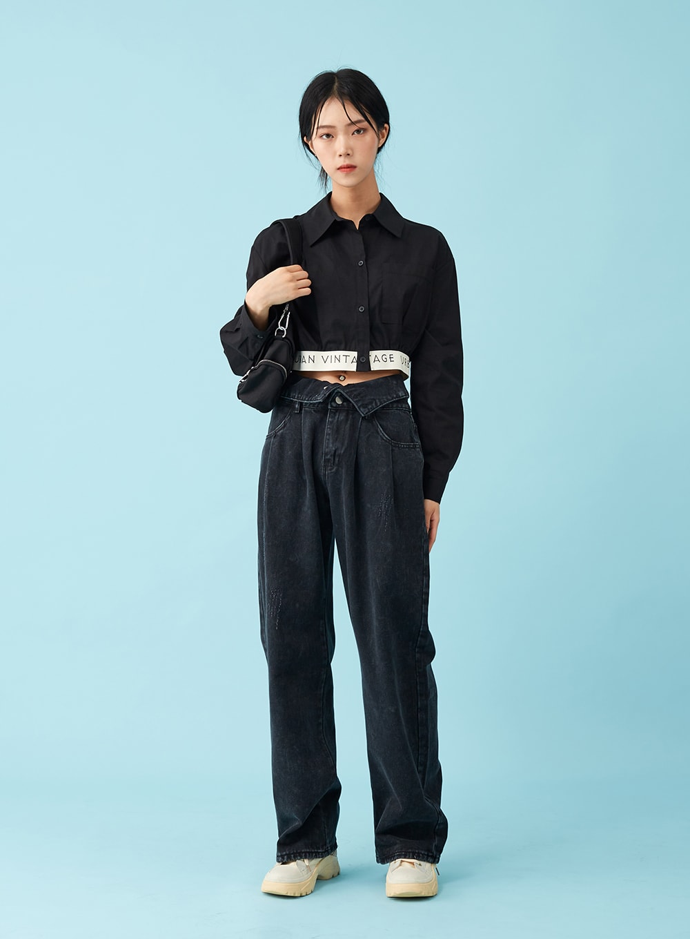 LEWKIN Four Buttoned Open Black Jeans CU8 in washed black, front full-body on model, wide-leg cotton denim with folded waistband detail, paired with black crop shirt and logo belt, chunky sneakers.