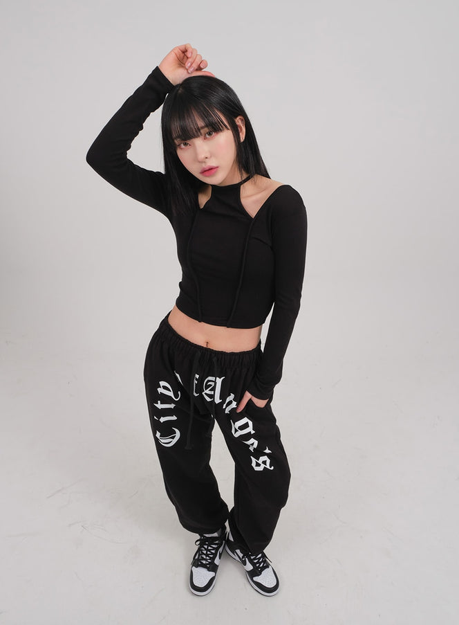 LEWKIN Cut Out Long Sleeve Top C0302 in black, angled front shot on model, slim crop fit with halter-neck cut-out detail, paired with black graphic sweatpants and sneakers.