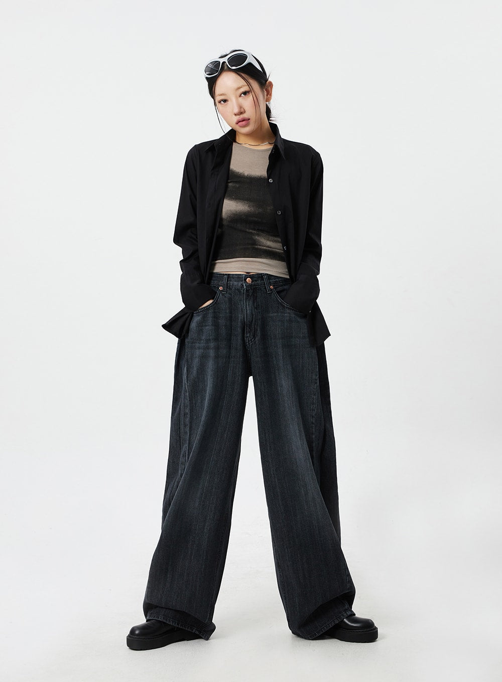 LEWKIN Mid-Rise Baggy Jeans CM324 in washed black denim, full-length front view on model, wide-leg silhouette pooling at hem, styled with black overshirt and graphic layering top.