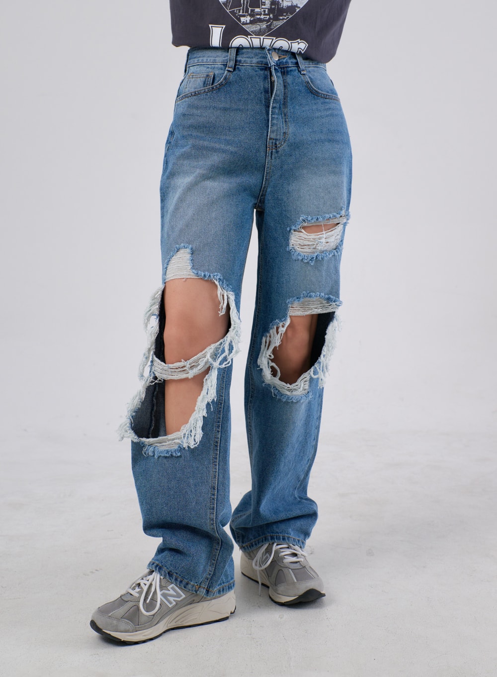 LEWKIN Ripped Knee Jeans IA305 in medium blue, front close-up on model, wide-fit cotton denim with oversized destroyed knee cutouts and frayed raw edges, paired with grey sneakers.