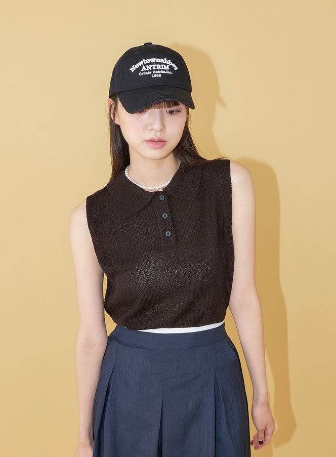 LEWKIN New Town Lettered Cotton Baseball Cap OU13 in black, front view on model, white embroidered lettering on crown, paired with dark knit vest and navy pleated skirt.