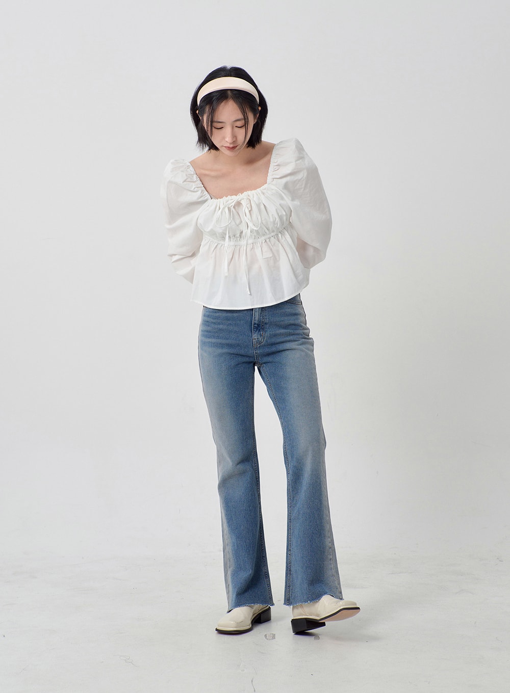 Light Washed Bootcut Jeans OD27 in light blue, front full-length on model looking down, slim-fit washed cotton denim, bootcut hem with raw edge, paired with white puff-sleeve blouse and white loafers.