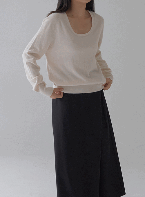 LEWKIN All Day Round Round Neck Knit in ivory, front three-quarter on model, soft knit U-neck sweater with ribbed hem, paired with black midi wrap skirt, hands on waist.