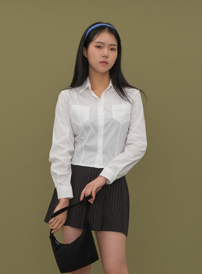 Cropped Shirt with Pockets C2601 in white, upper-body front close-up on model, slim fit with corset-style seam lines and dual chest pockets, styled with pinstripe mini skirt.