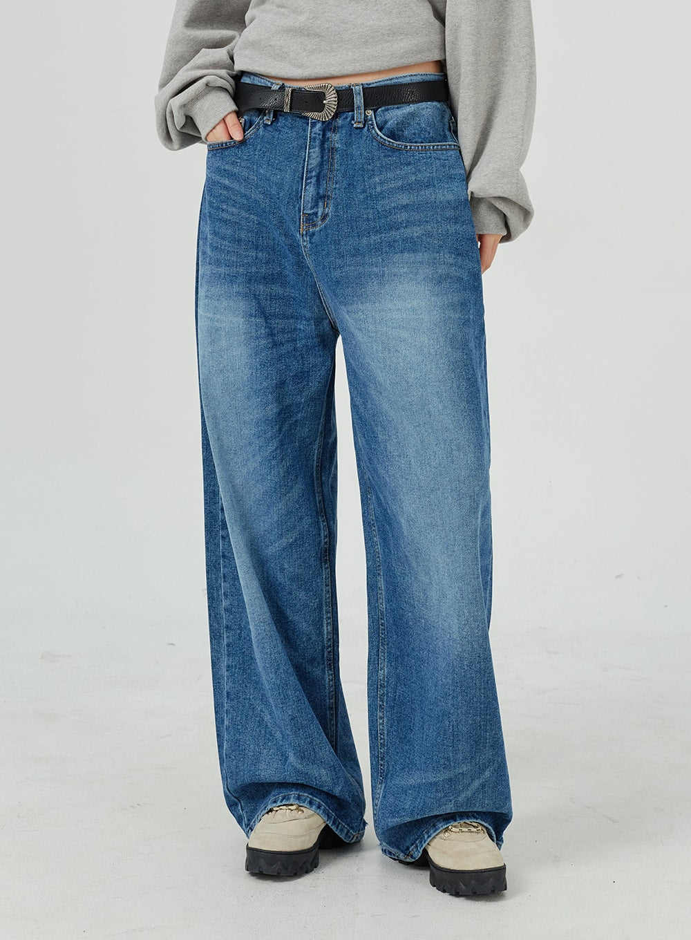 Oversized Jeans Unisex CM321 in blue, waist-to-hem front close-up, wide-leg denim with washed fading and front pockets, styled with black western belt.